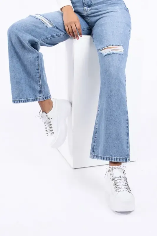 vertical shot female model wearing blue wideleg torn jeans with white trainers
